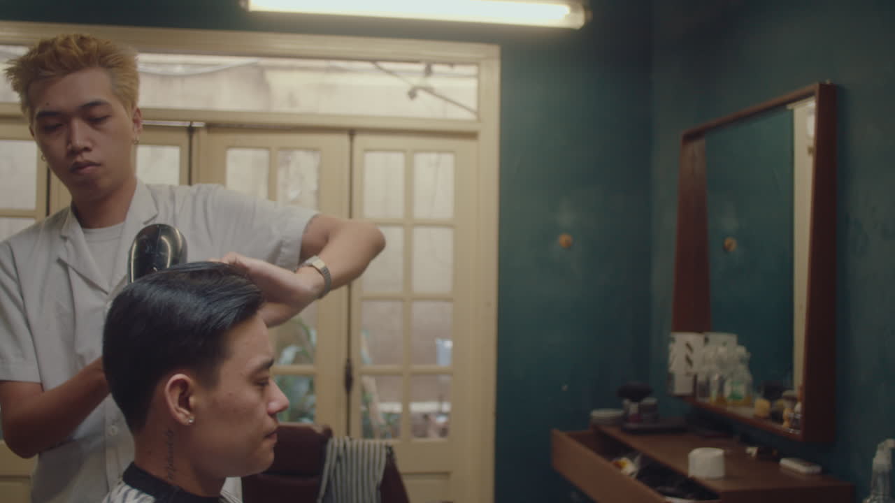 Asiatisk barber føntørrer mandlig kundes hår