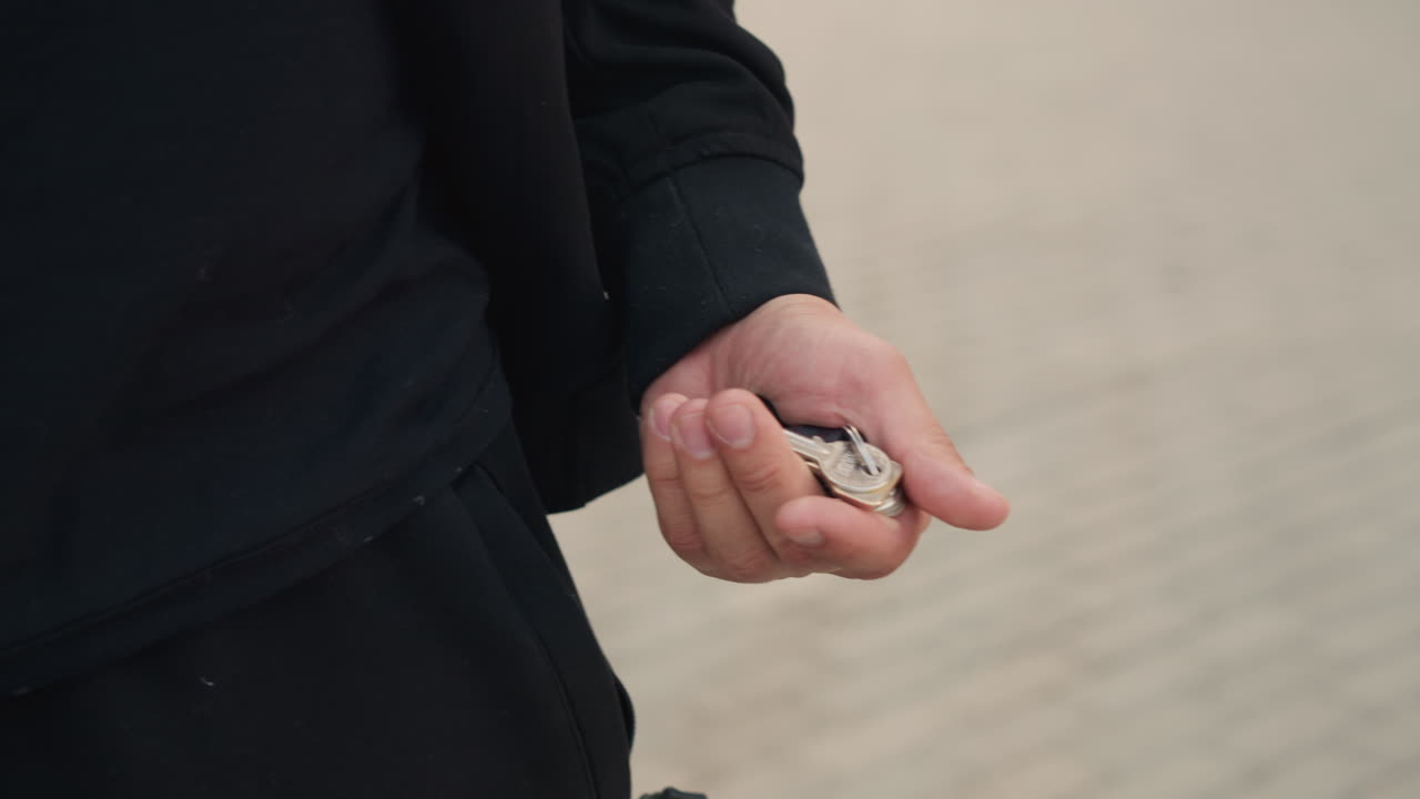 さりげなく差し出される鍵、近くに鍵を持って手を伸ばすカジュアルな手、日中に鍵を差し出す手の写る親しみやすい屋外の風景、ポケットの近くで鍵を伸ばした手の写るリラックスした瞬間。