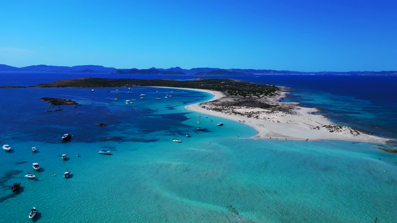 Espalmador island featuring white sand beaches, clear turquoise water, and anchored boats. Ibiza and the island of Es Vedra in the background. Smooth aerial view flight panorama overview drone