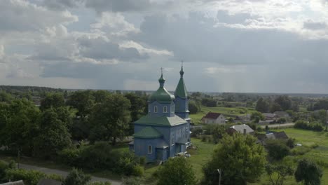 a beautiful church in ukraine with green trees and various houses and cloudy skies - aerial shot