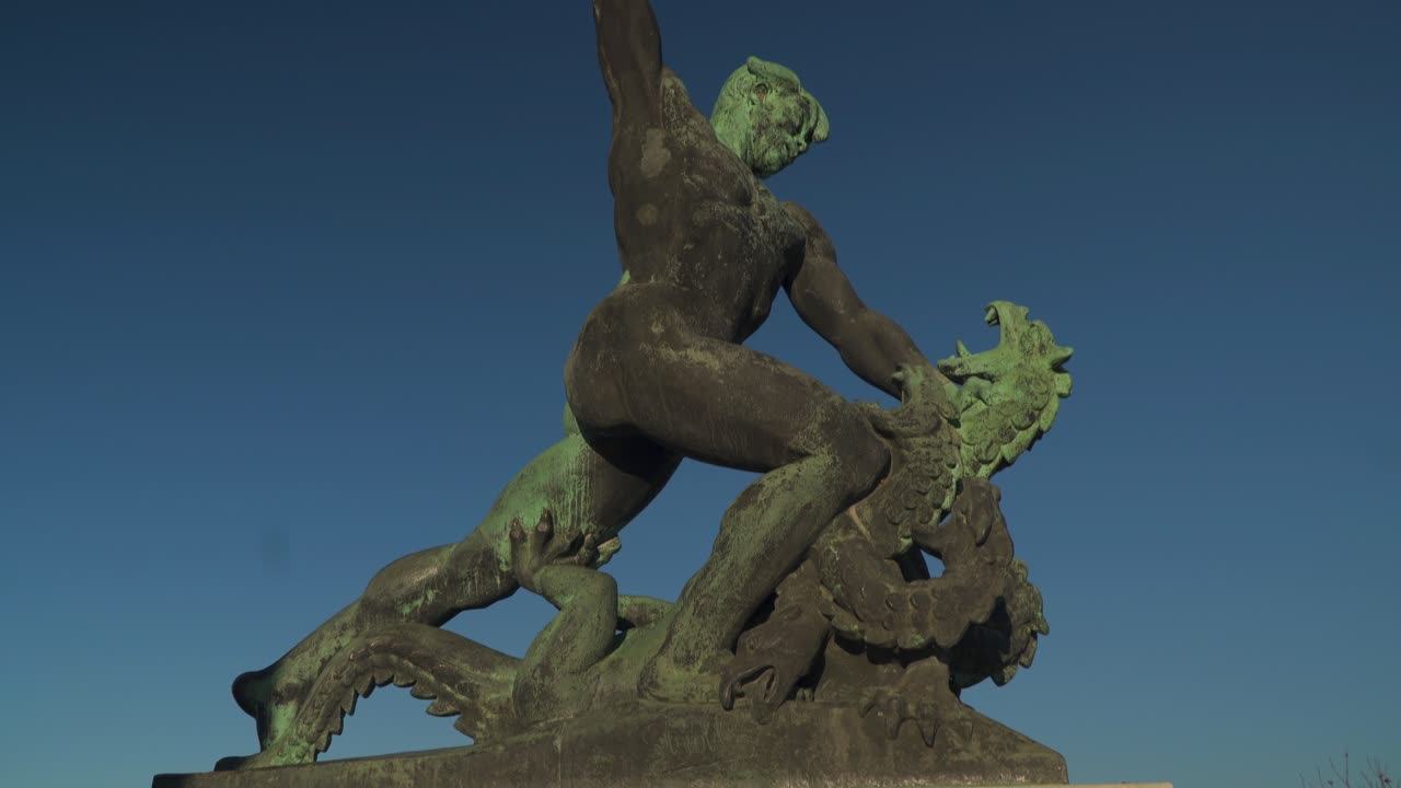 Statue of a Hungarian warrior fighting a three-headed dragon on top of Gellert Hill, Budapest, Hungary With Blue Sky - Tilt Down Shot