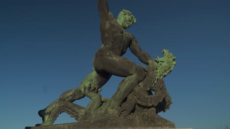 statue of a hungarian warrior fighting a three-headed dragon on top of gellert hill, budapest, hungary with blue sky - tilt down shot