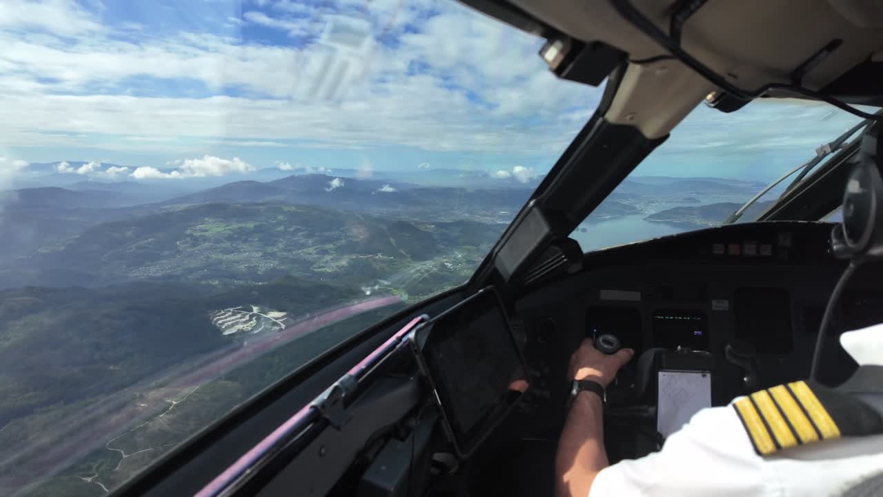 An immersive pilot’s perpective, Captain seat, flying a jet airplane at low altutude through some frayed clouds and over a montainous landscape.