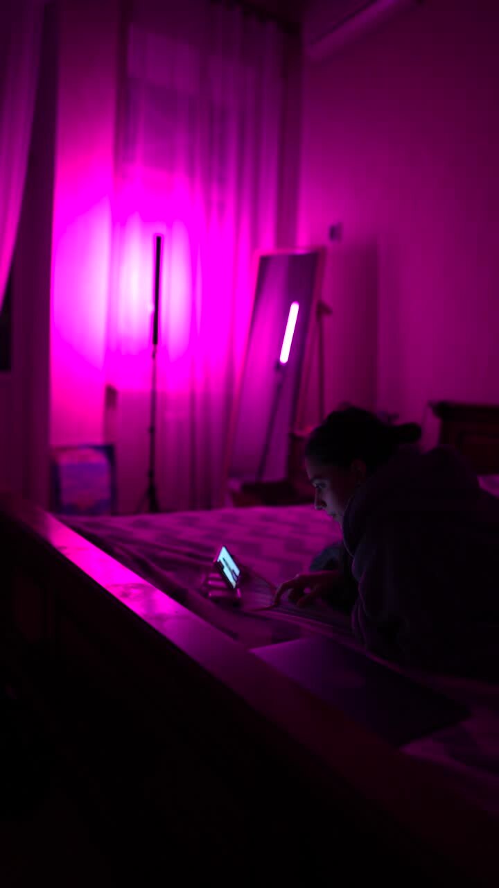 Donna che usa il telefono in una camera da letto illuminata di viola di notte