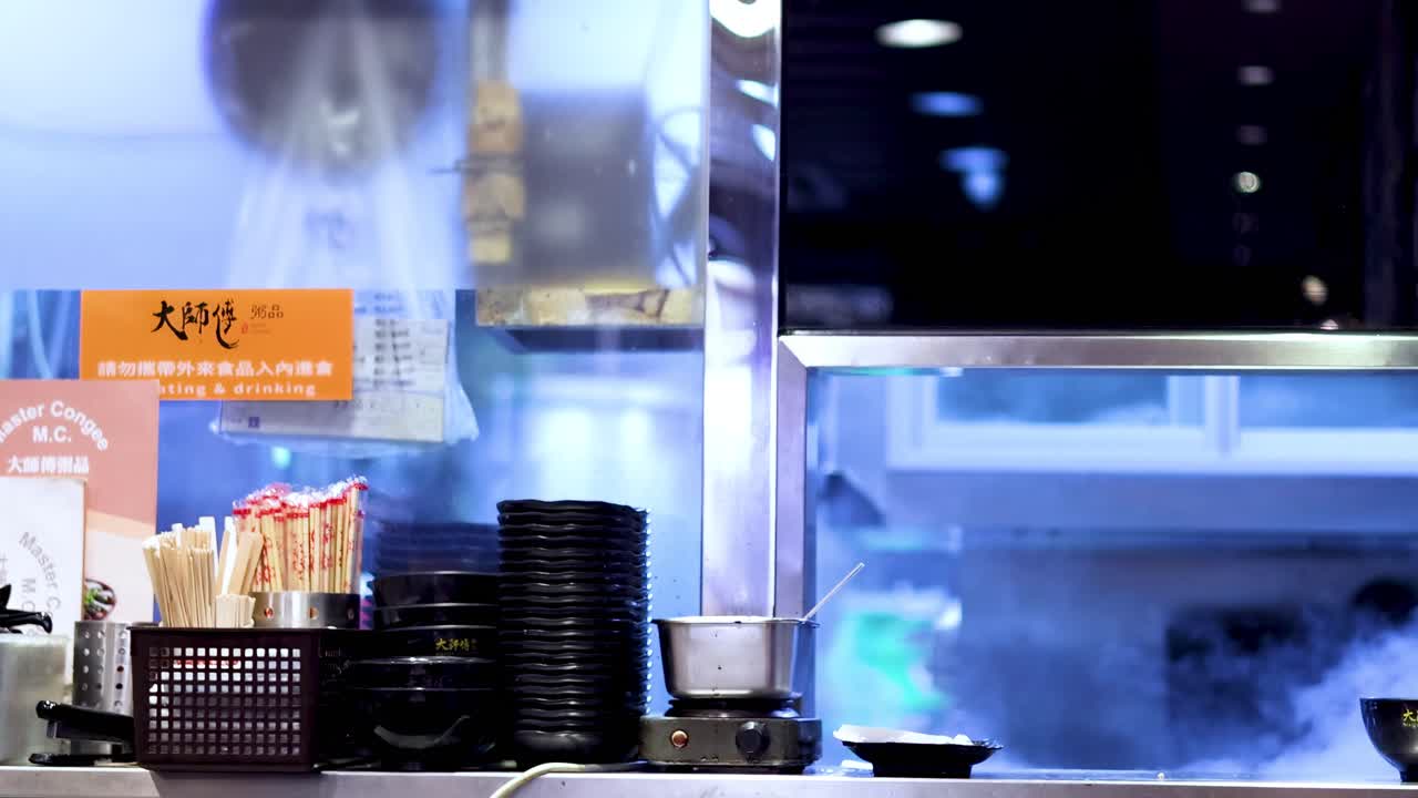 A vibrant kitchen counter with stacked plates, chopsticks, and rising steam, showcasing a dynamic cooking environment.