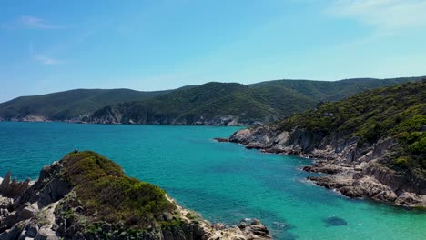 Aerial-view-of-turquoise-blue-crystal-clear-water-and-rocky-coast-line-with-island-view-discovering-while-flying-backwards