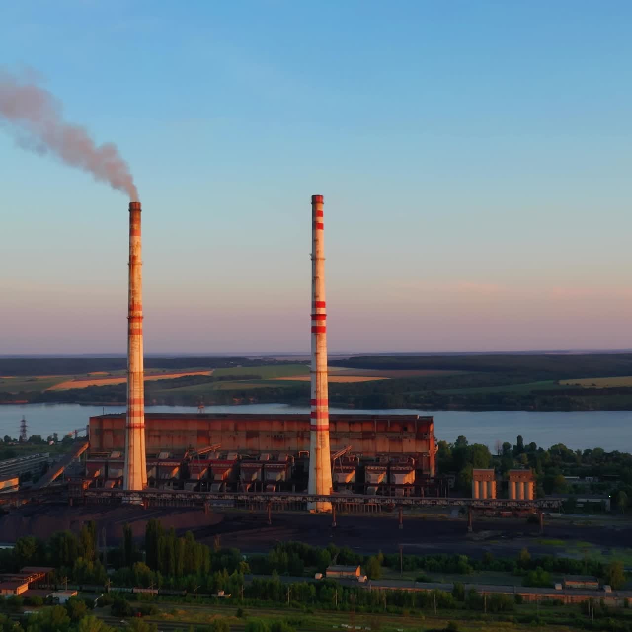 Industrial zone with chimneys at sunset. Panoramic view on pipes with smoke of factory on nature background. Environmental pollution.
