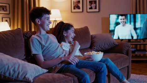 kids laughing and eating popcorn while watching tv at home
