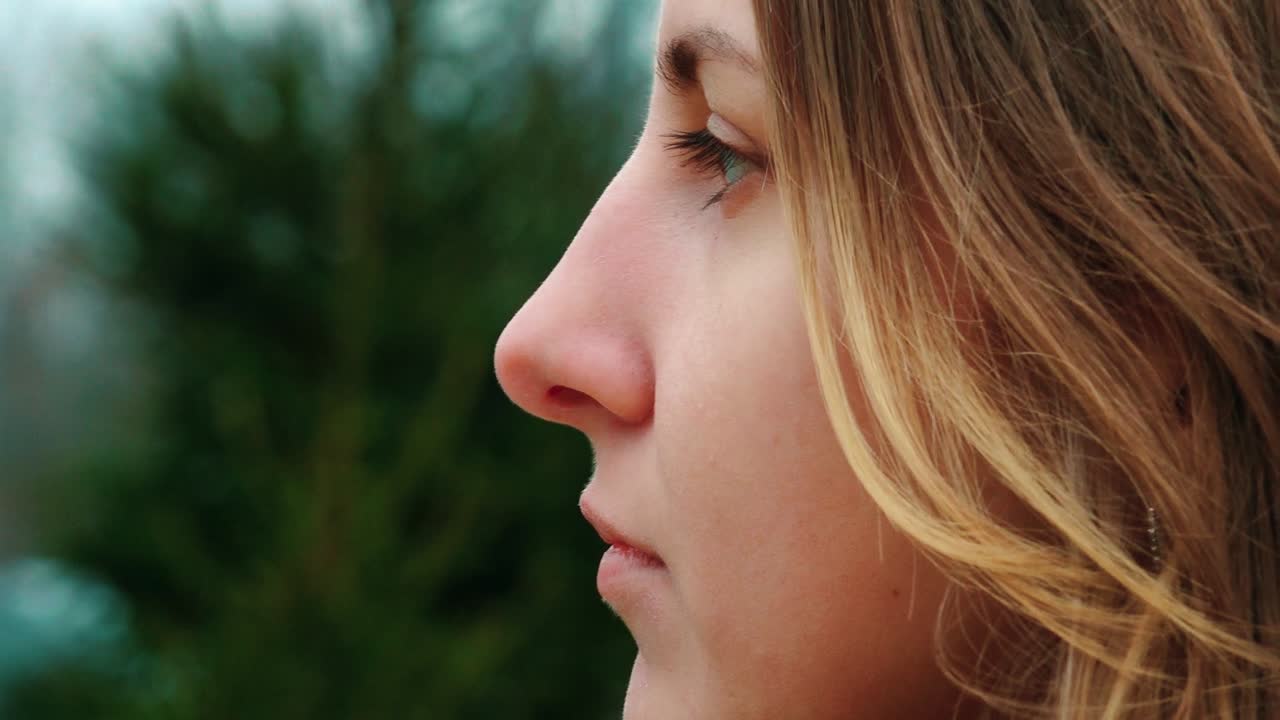 vista de perfil en primer plano de una mujer con cabello rubio contra un fondo desdibujado al aire libre. el enfoque está en sus rasgos faciales y expresión serena.