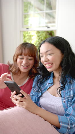 vertical video: smiling friends using smartphone and relaxing at home, enjoying time together