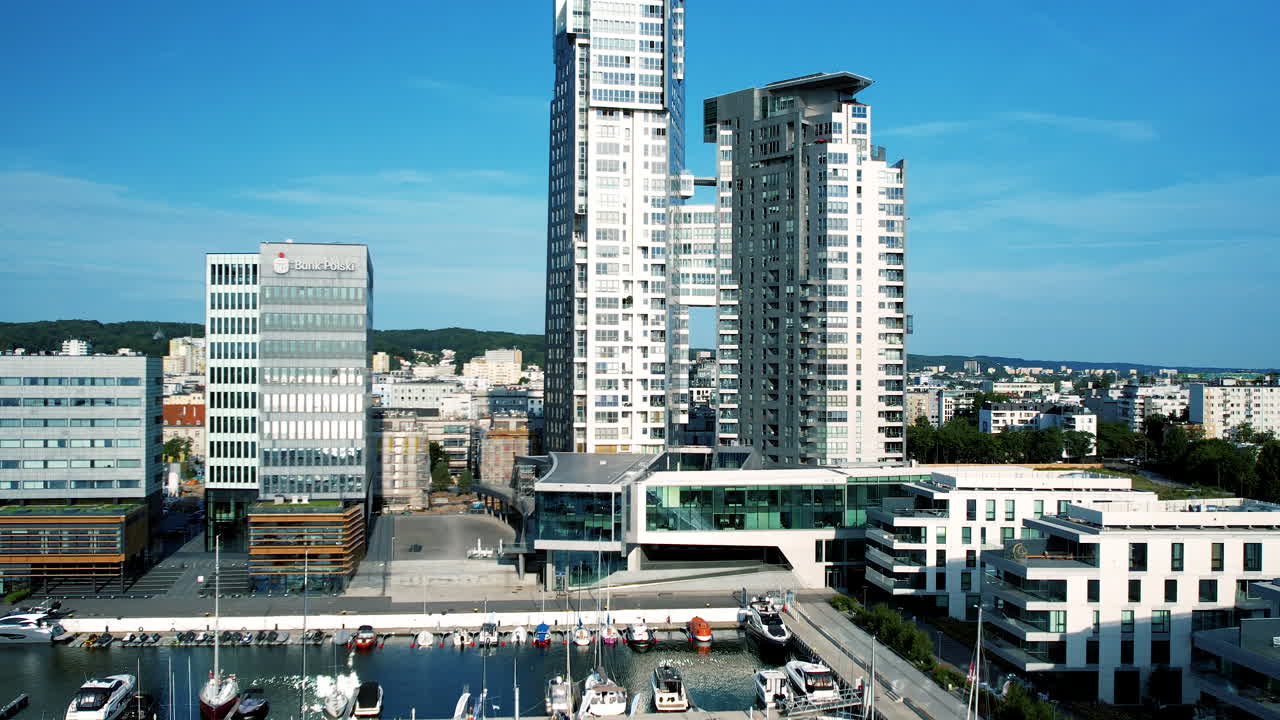 Ocean view modern apartment building looks over pier and boats on blue sky day
