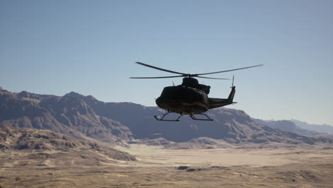 a helicopter flying over a desert landscape with mountains in the background