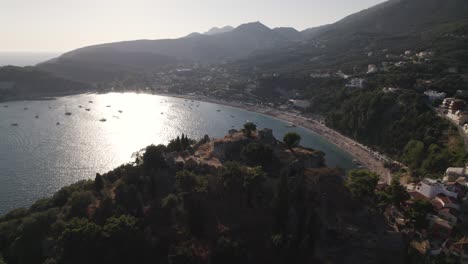 Aerial-Cinematic-Flying-Over-Hillside-With-Parga-Castle-With-Sunshine-Reflected-Of-The-Ionian-sea