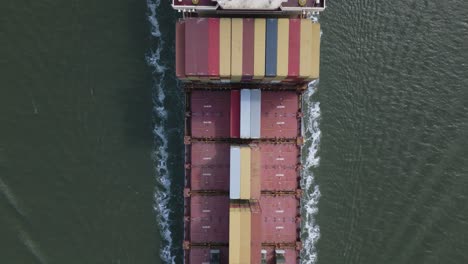 Container-ship-loaded-passing-by,-leaving-trail-of-foam-in-water
