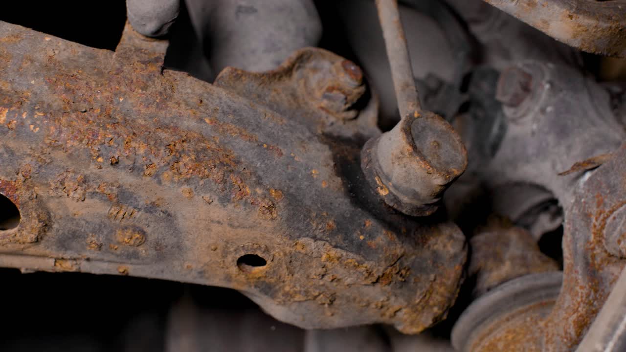 Close up of the rusty front suspension underneath a used car. Sideways pan shot with movement in 4k.