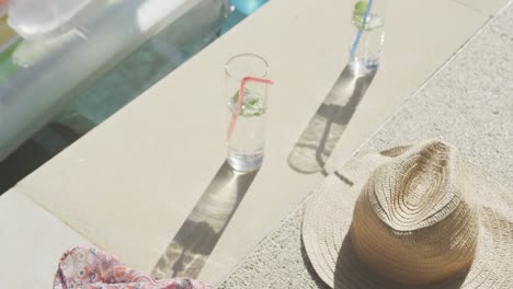 Straw-hat,-drinks-and-inflatables-in-swimming-pool-in-garden-on-sunny-day