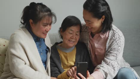 smiling senior asian woman using smartphone with adult daughter and granddaughter embracing