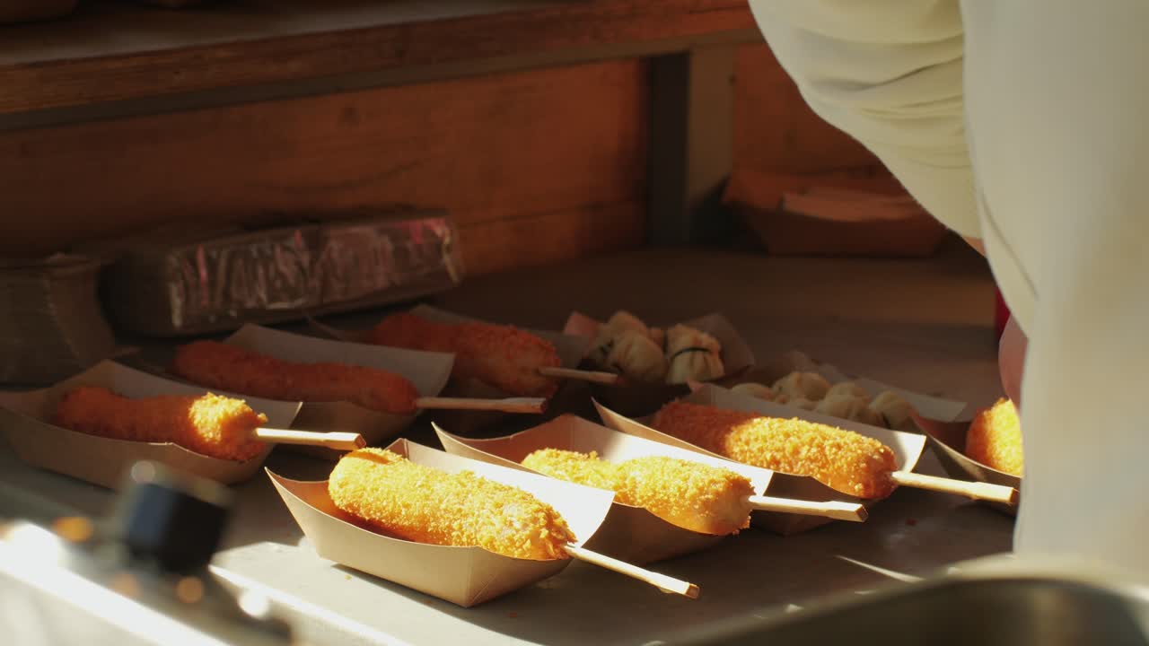 Cooking corn dogs in boiling oil close-up. Traditional asian corndog snacks street food. Fried sausage in breadcrumbs on a stick. Korean Chinese street local market with traditional food. American fast food corndogs with sauce on the top. High quality 4k footage