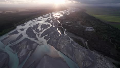 volando sobre el río trenzado waimakariri hacia la puesta de sol con rayos de luz en christchurch, canterbury nueva zelanda