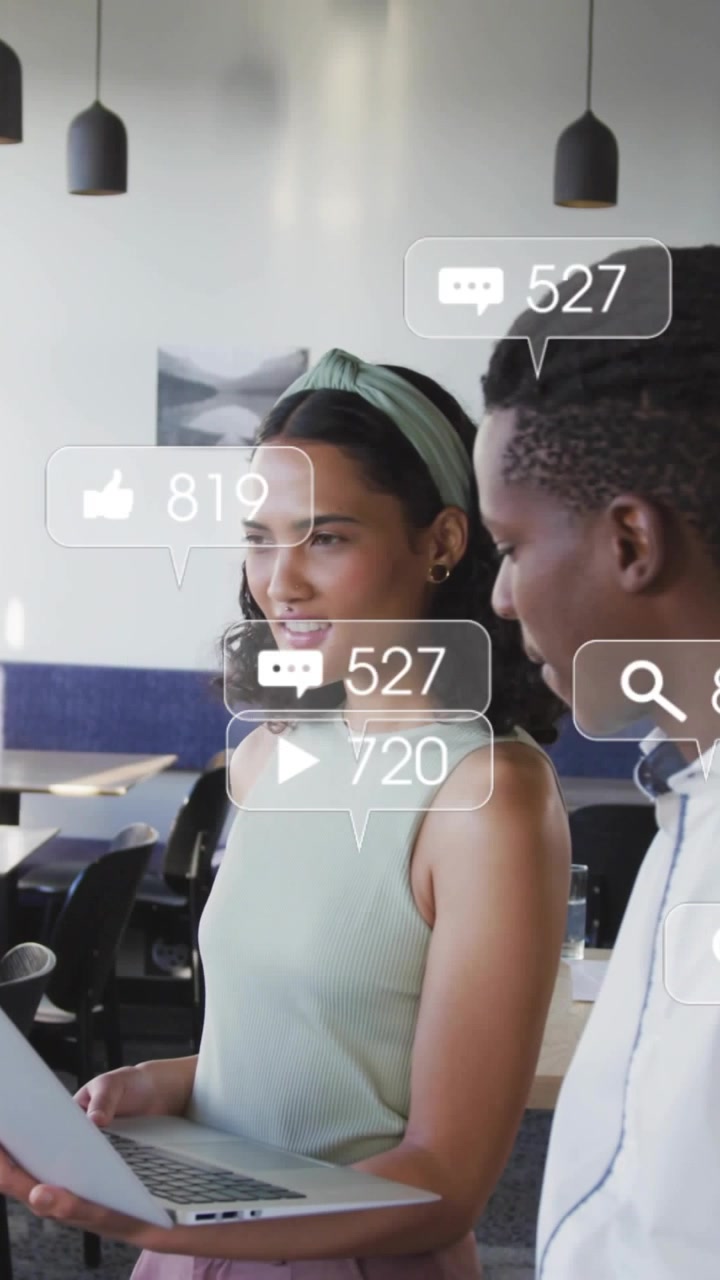 Vertical video: Woman showing laptop causing social icons while man leaning checking KPIs for ads