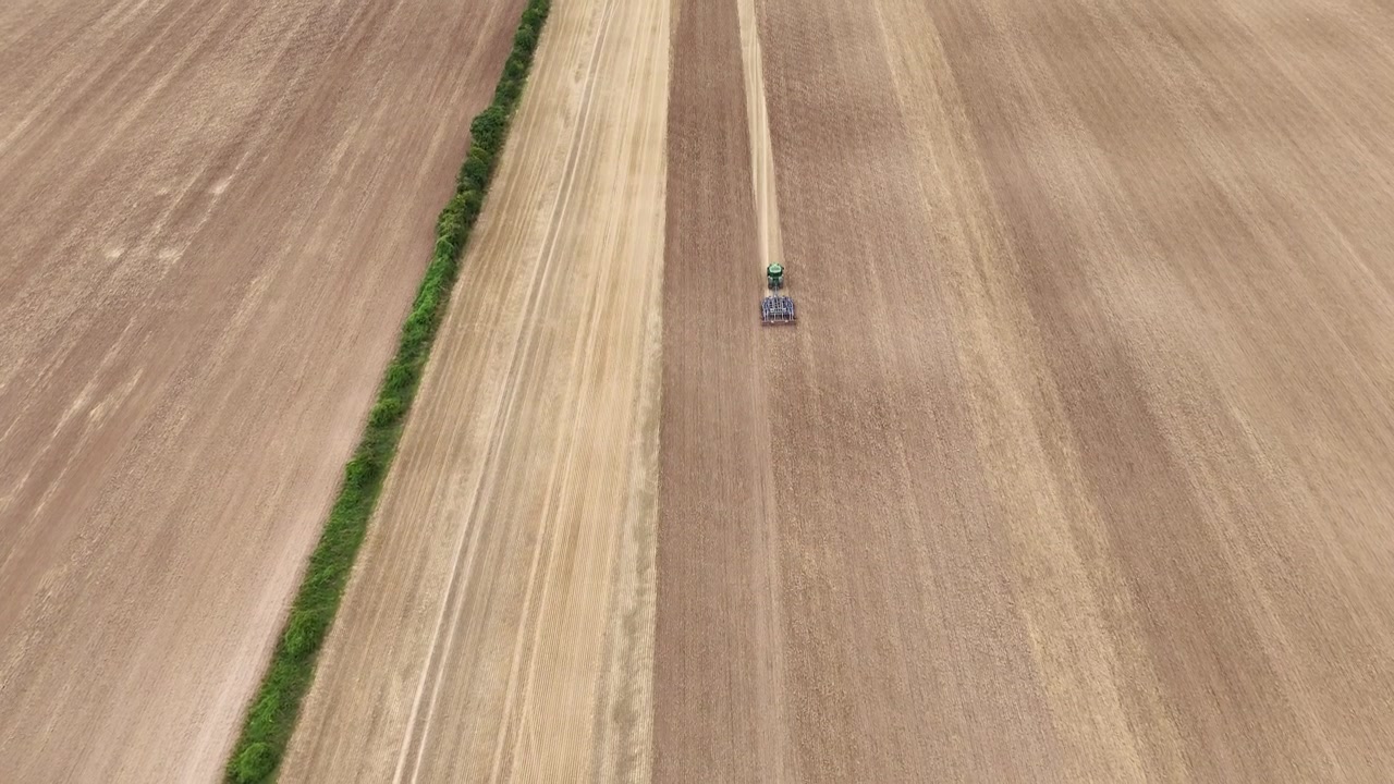 Panoramisk flygvy uppifrån av en traktor som arbetar på fältet i Etchilhampton, Storbritannien, och lämnar definierade linjer i den skördade marken.