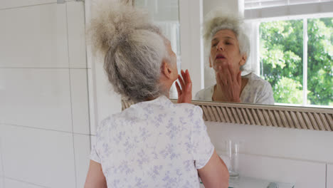 Caucasian-senior-woman-touching-her-face-while-looking-in-the-mirror-at-home