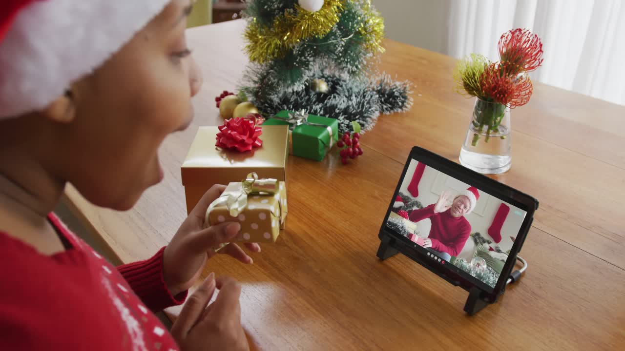 mujer afroamericana con sombrero de santa usando tableta para videollamada de navidad, con hombre en la pantalla
