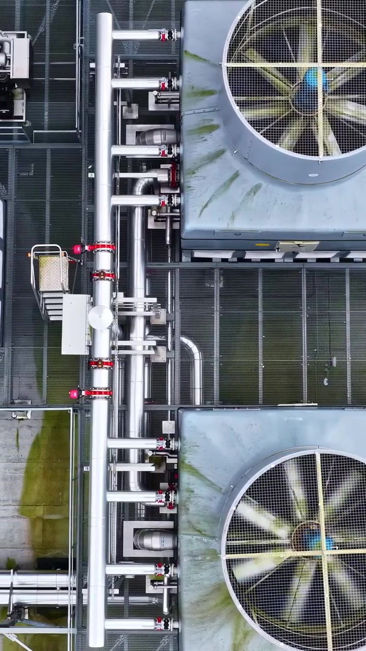 Aerial view of large industrial cooling fans rotating on a rooftop with visible piping
