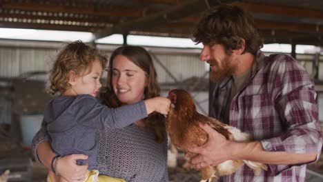 familia caucásica feliz trabajando en una granja, manteniendo pollo