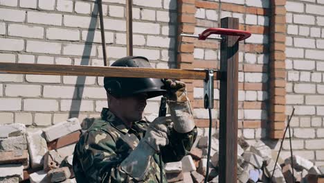 worker in camouflage welds and checks little detail of fence