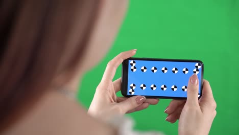 mujer sostiene un teléfono inteligente en orientación horizontal con marcadores de seguimiento en la pantalla y deslizando hacia la izquierda