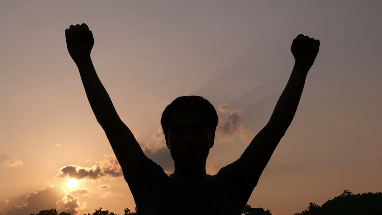 Silhouette of a person with arms raised at sunset