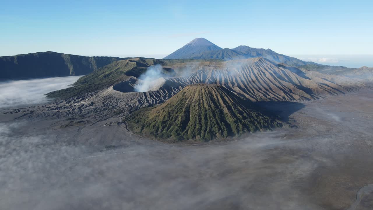 Scenic panoramic shot of Bromo Tengger Semeru National Park, showing volcanic peaks, ridges, and fog drifting across caldera at sunrise