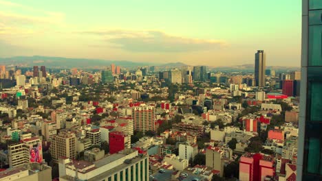 Drone-revealing-cityscape-behind-tall-building-urban-neighborhood-Mexico-City-morning-light-clear-sky