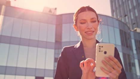 ejecutivo sonriente enviando mensajes de texto por teléfono móvil en el distrito de negocios soleado de cerca.