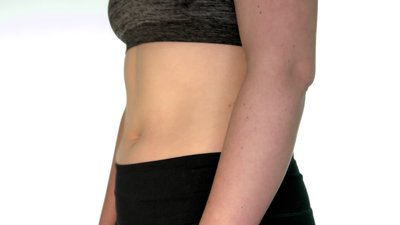 Side view of a young woman's belly with visible fat. The belly is undulating. Diet and weight loss concept