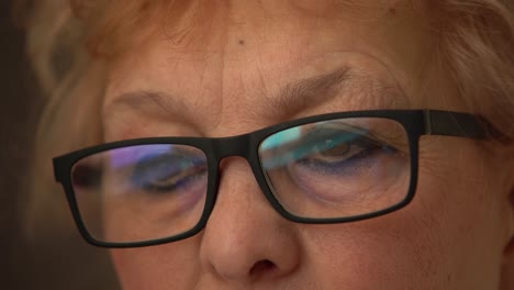 close up: elderly woman with glasses working on pc. eyes reflecting monitor