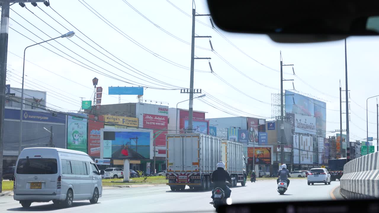 Daytime traffic with vehicles and motorcycles navigating a busy intersection in Phuket, Thailand, under clear skies