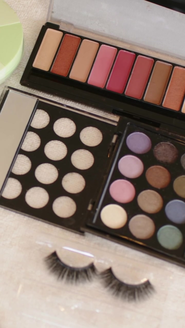 Vertical video: Tilting camera showing palettes and false lashes on towel, revealing amber bottles