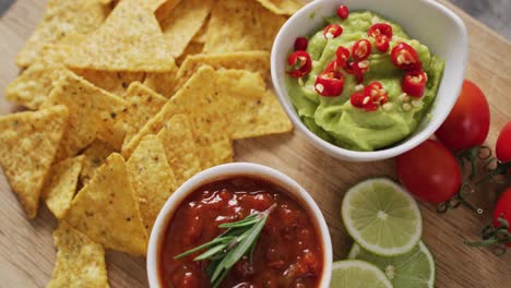 close up of nachos and sauces on wooden tray on black surface