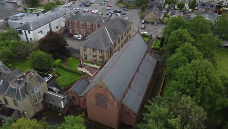 Aufsteigende-Luftaufnahme-über-Die-Von-Bäumen-Umgebene-Kirkintilloch-Kirche,-Die-Den-Rest-Der-Gebäude-Und-Den-Horizont-Im-Hintergrund-Freigibt