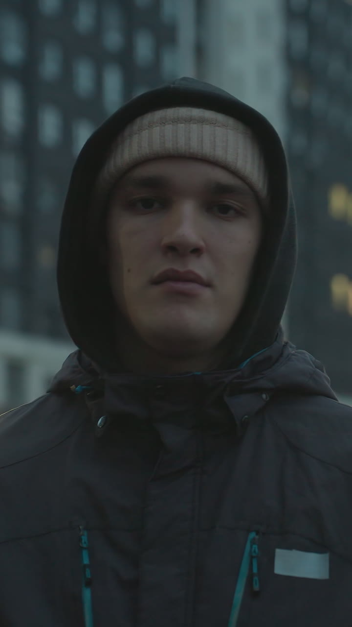 hombre con capucha y gorra realizando control de pelota con una pelota de fútbol durante una sesión de entrenamiento urbano, mostrando enfoque y habilidad contra el telón de fondo de altos edificios residenciales y cielo nublado por la noche