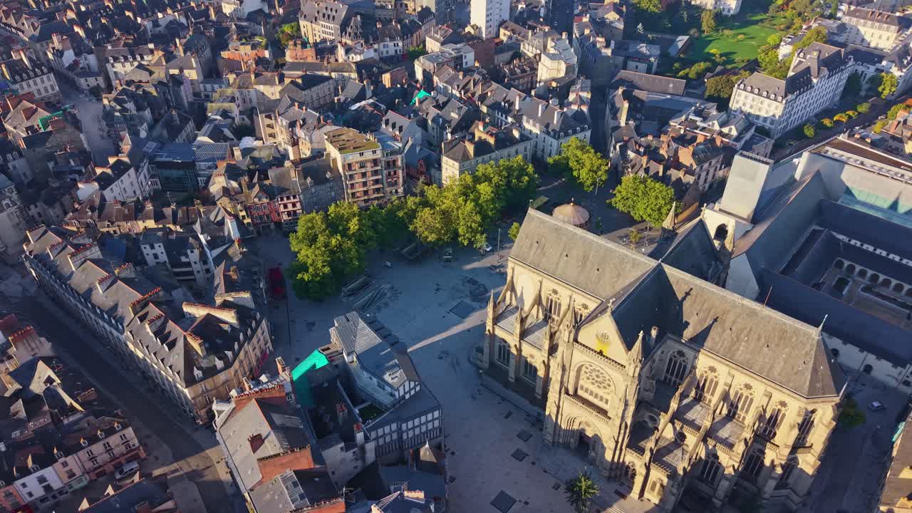 Drone panning over Place Sainte-Anne at sunrise, showing the Basilica Notre-Dame de Bonne-Nouvelle, the Jacobins convent and the historic center of Rennes in a high-angle view