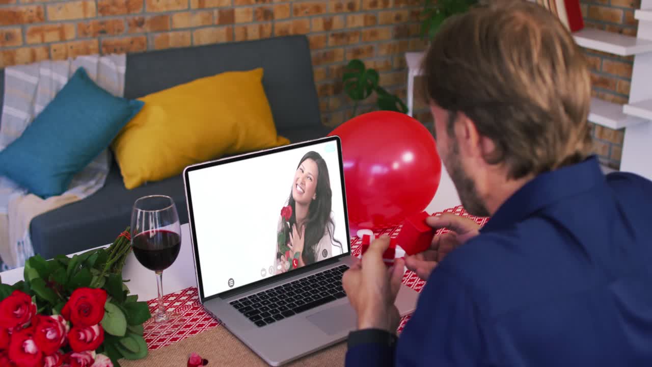 Casal caucasiano em videochamada de Dia dos Namorados, homem mostrando anel para mulher sorrindo na tela do laptop.
