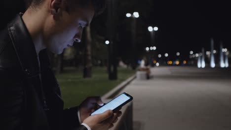 hombre usando un teléfono inteligente por la noche en el parque