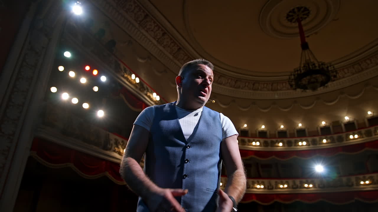 Man on stage gesticulating and talk. Professional actor performing his role on spotlight background in theater. View from stage.