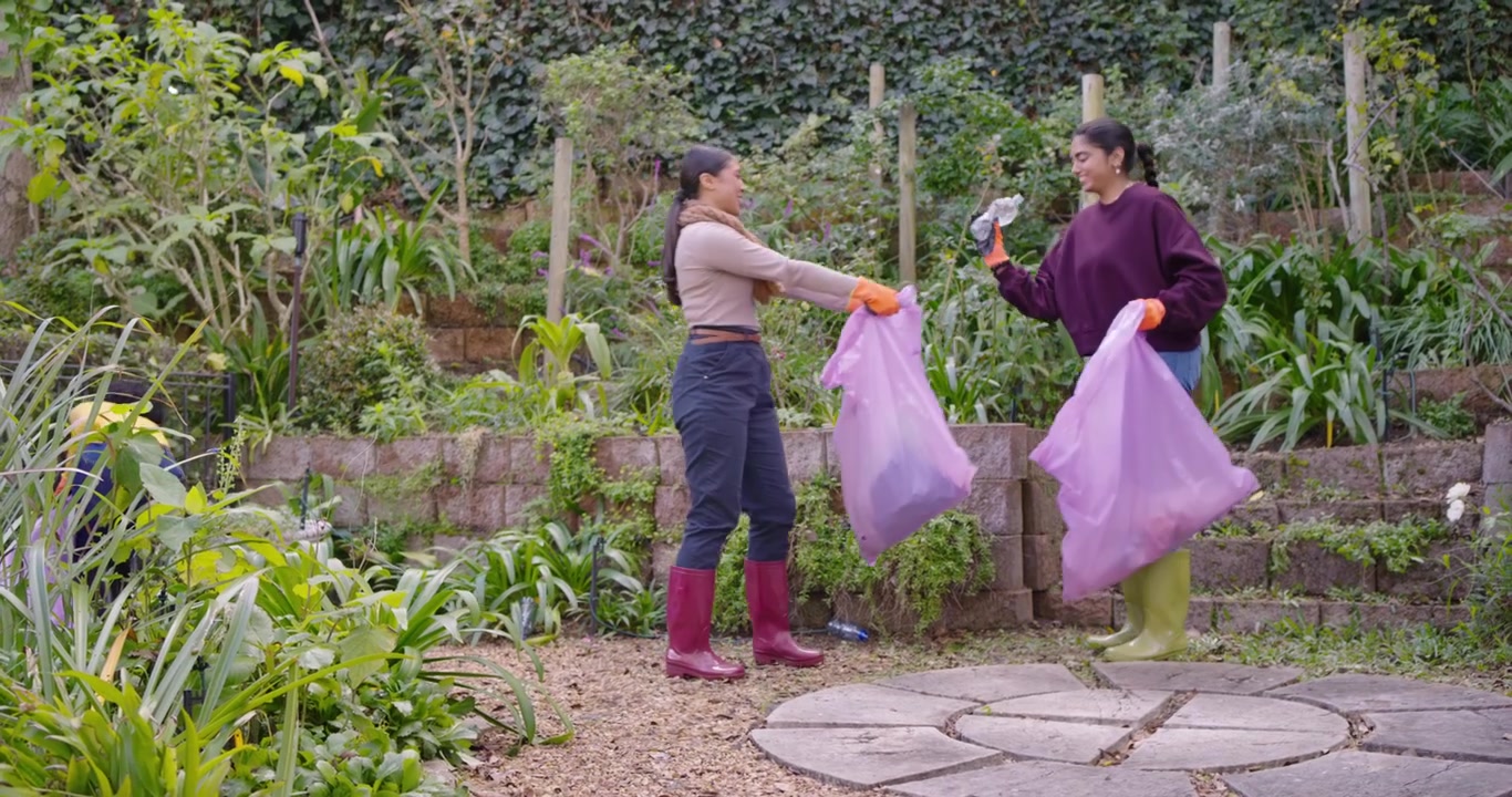 Diverse women arriving in garden, picking litter with grabber and orange gloves, filling pink bags