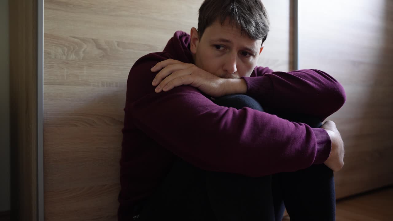 hombre blanco caucásico se sienta con las piernas contra el pecho de vuelta a la pared triste arrepentido de las elecciones deprimido