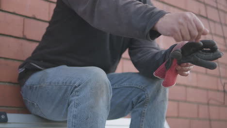 Trabajador-Sentado-Mientras-Sostiene-Guantes-De-Trabajo-Y-Hace-Gestos-Con-La-Mano-Durante-El-Descanso-Del-Trabajo---ángulo-Bajo,-Cierre