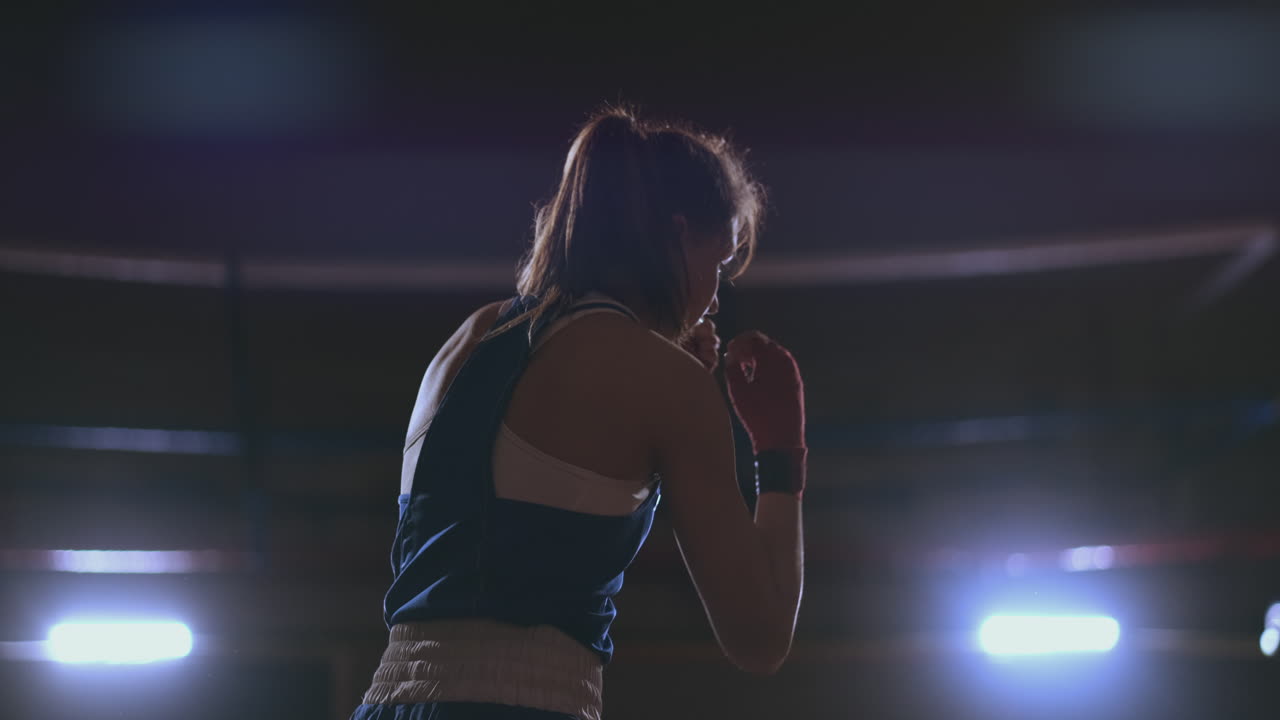 Pugile donna che si allena in una stanza buia con controluce al rallentatore. Ripresa steadicam.